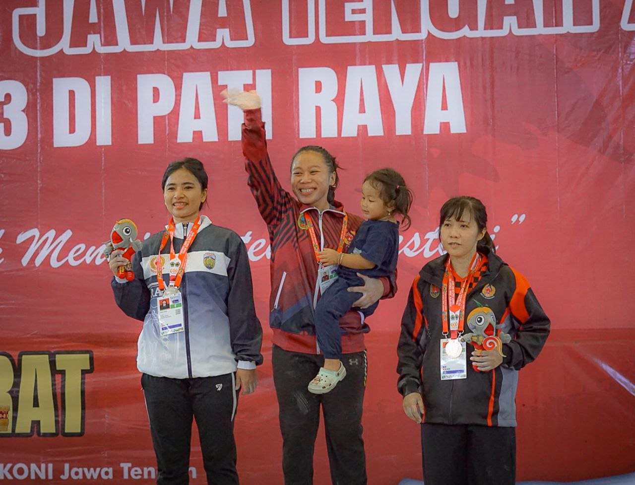 Foto : Laila Rahmawati sambil gendong sang anak terima medali emas dari cabor Angkat Berat Kelas 63 Kg Putri di ajang PORPROV XVI Tahun 2023 (Sumber : pesantenanpati.com/ Anang SY)