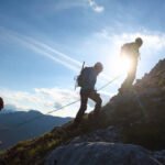 Three mountain climbers silhouettes against a blue sky with sun.